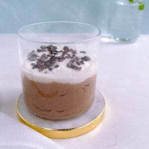 glass of mint chocolate overnight oats garnished with cacao nibs on a white and gold coaster