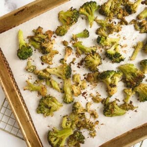 gold sheet pan lined with parchment paper containing oil-free roasted broccoli