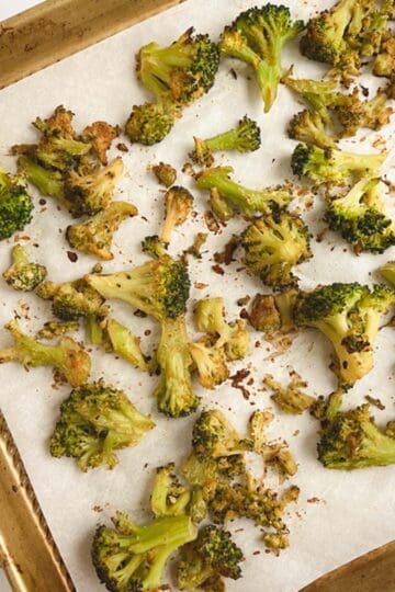 gold sheet pan lined with parchment paper containing oil-free roasted broccoli