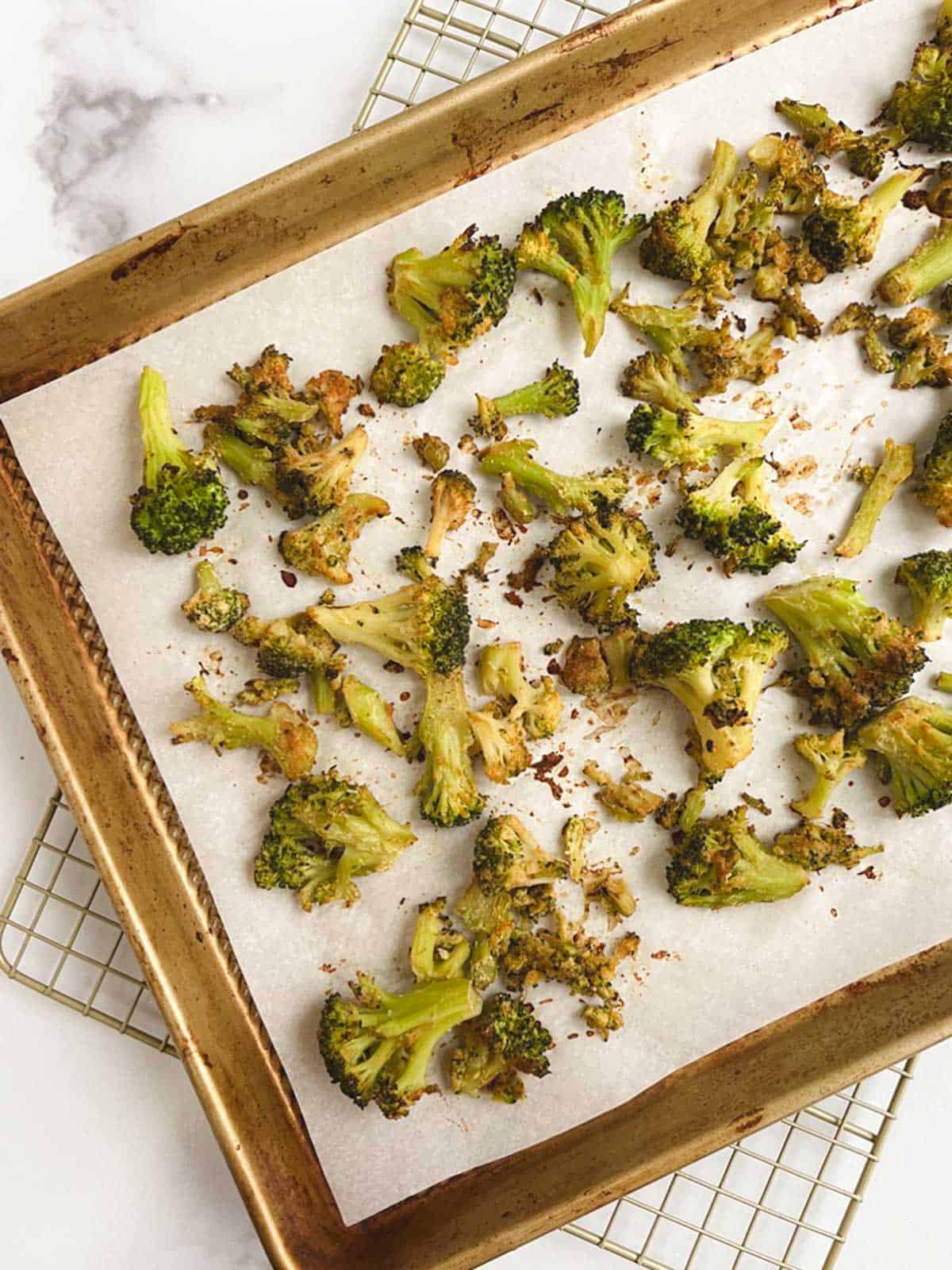 gold baking sheet lined with parchment paper containing oil-free roasted broccoli on a white marble countertop