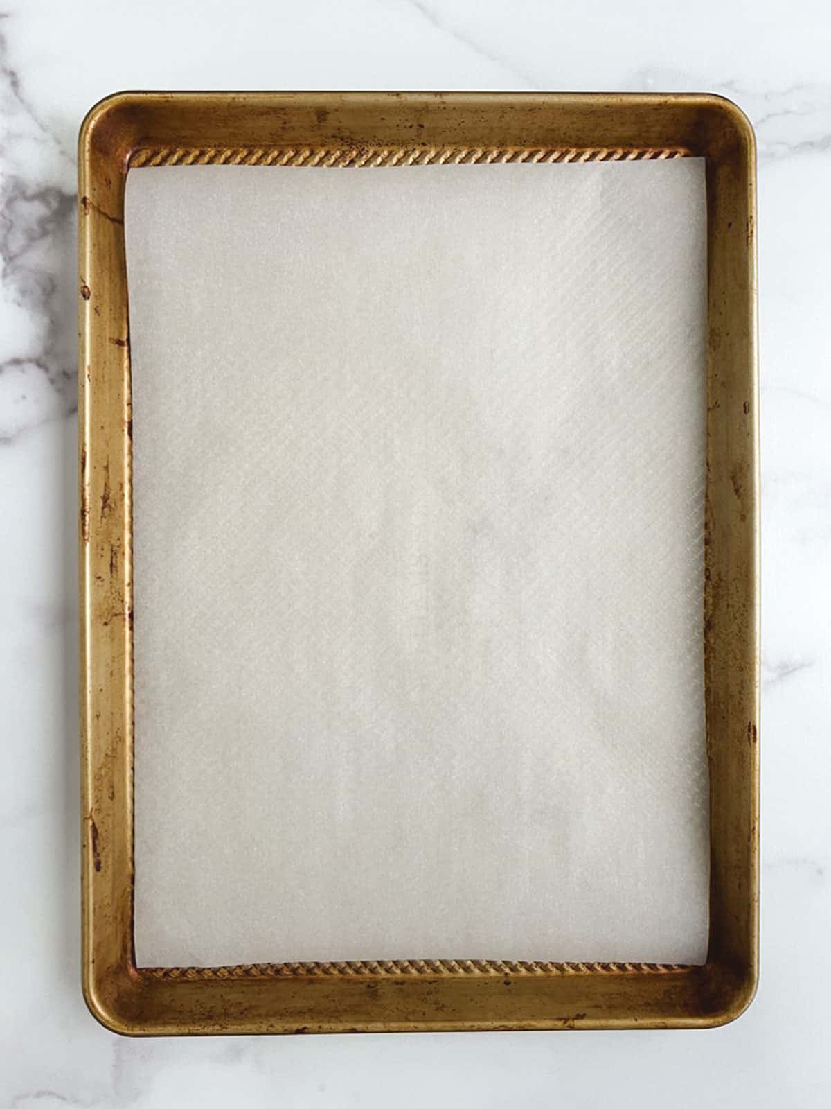 gold baking sheet lined with parchment paper on a white marble countertop