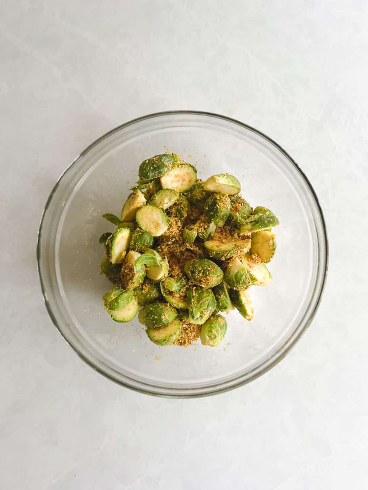 overhead view of glass bowl containing Brussels sprouts tossed with seasoning