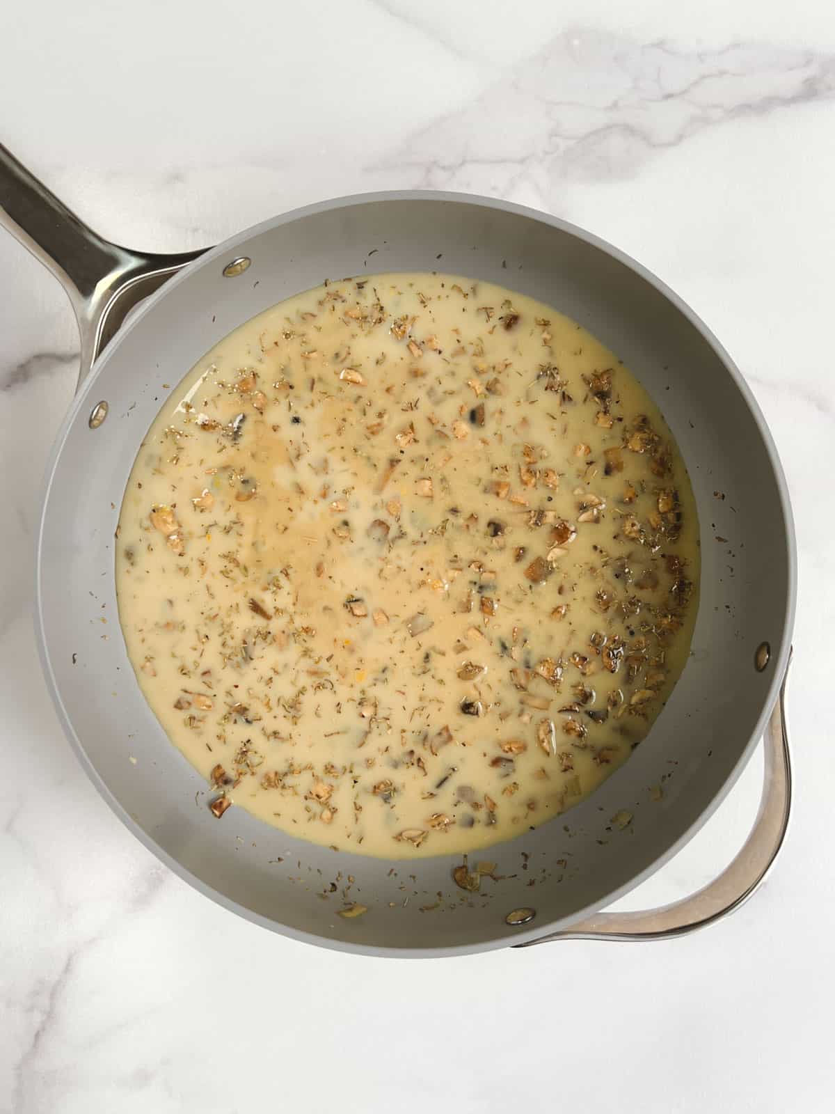 overhead view of skillet containing cooked vegetables with broth, soy milk, tamari, miso, nutritional yeast, thyme, and pepper added