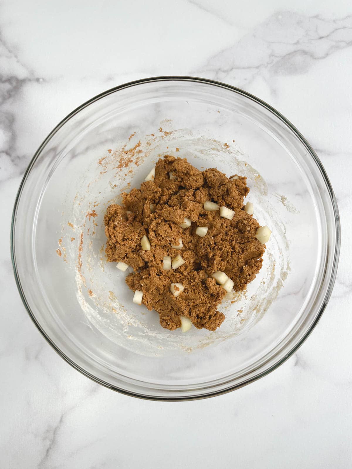 overhead view of glass bowl containing combined wet and dry ingredients with pear chunks stirred in