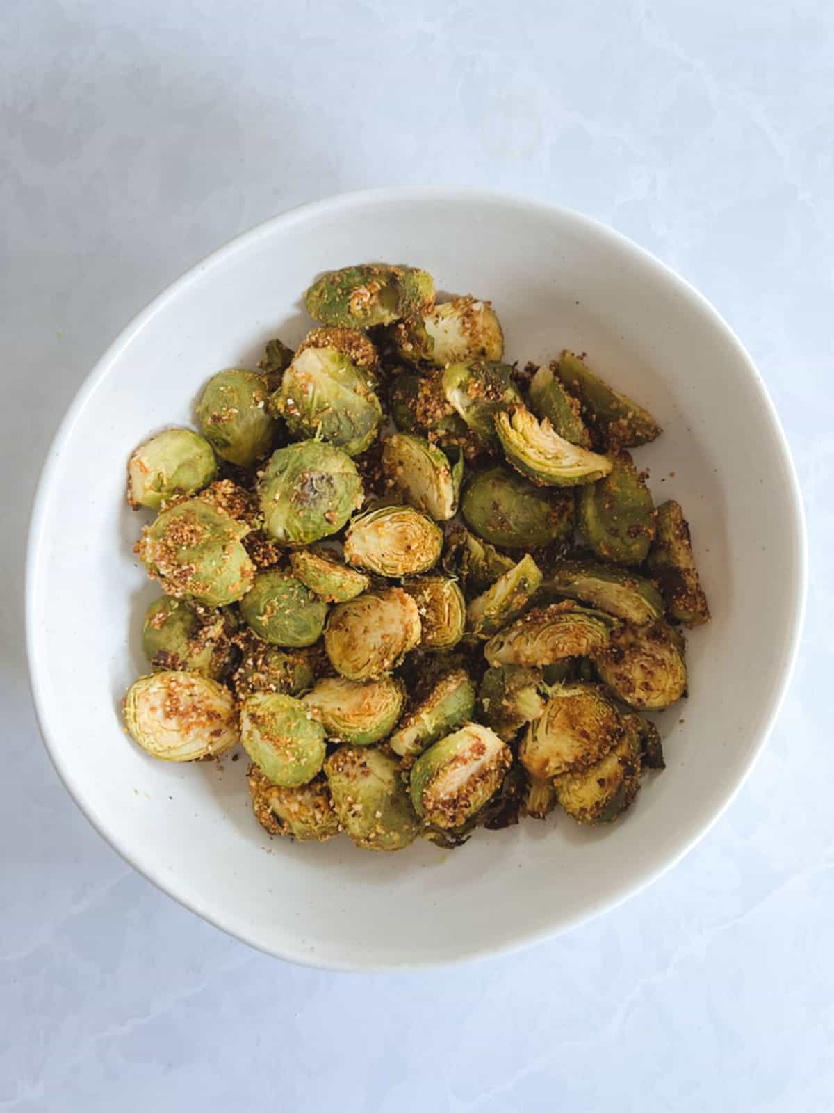 overhead view of white bowl containing crispy Brussels sprouts roasted in the oven