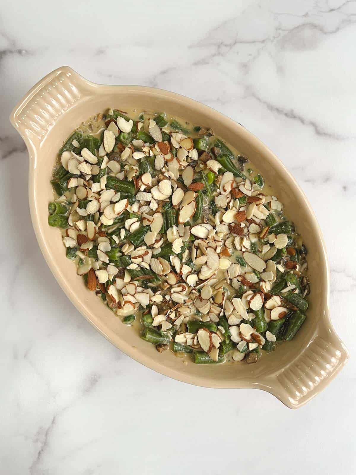 overhead view of oval casserole dish containing uncooked vegan green bean casserole topped with raw almonds