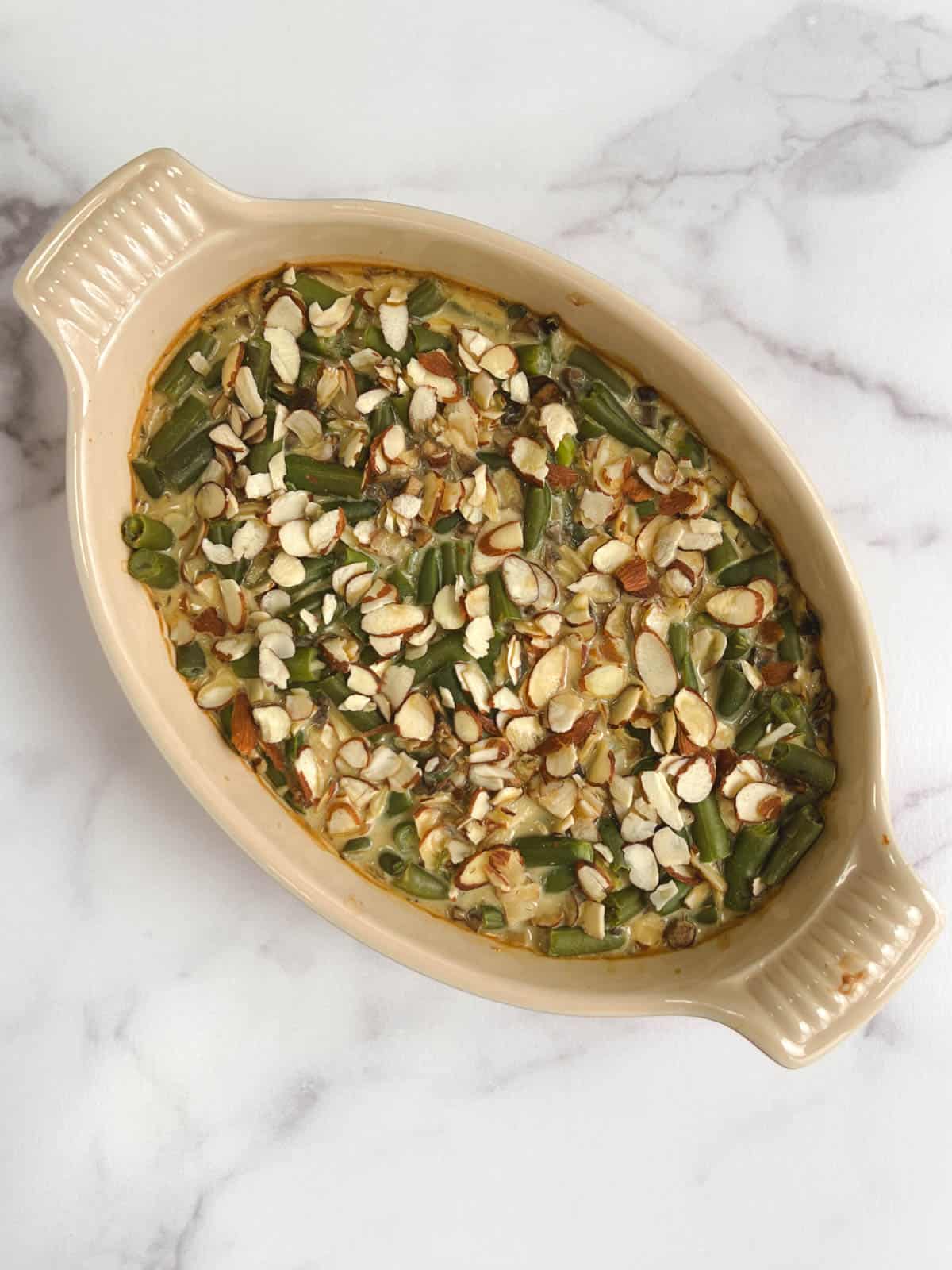 overhead view of oval casserole dish containing cooked vegan green bean casserole topped with toasted almonds