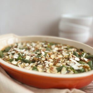 orange oval serving dish containing vegan green bean casserole with white bowls stacked in background