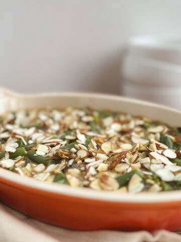 orange oval serving dish containing vegan green bean casserole with white bowls stacked in background