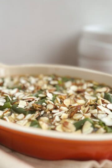 orange oval serving dish containing vegan green bean casserole with white bowls stacked in background