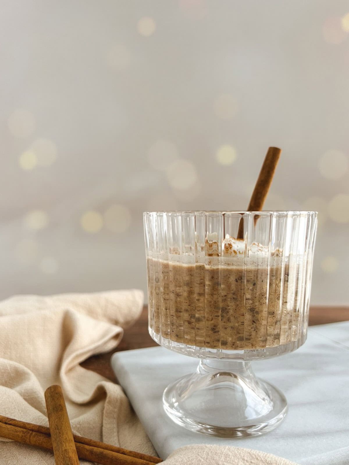 closeup of parfait glass containing chai overnight oats garnished with a cinnamon stick, with a linen napkin and cinnamon sticks to the side