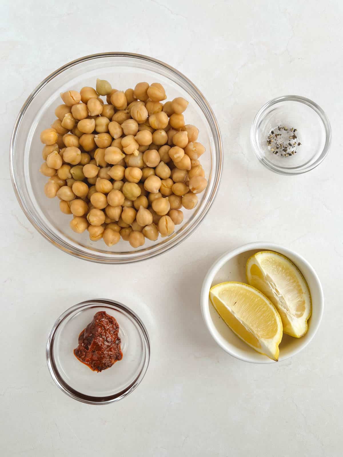 overhead view of ingredients for harissa chickpeas in bowls on a cream-colored background