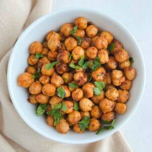 overhead view of white bowl containing harissa chickpeas with a beige napkin draped to the left