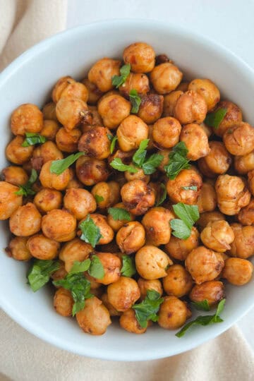 overhead view of white bowl containing harissa chickpeas with a beige napkin draped to the left