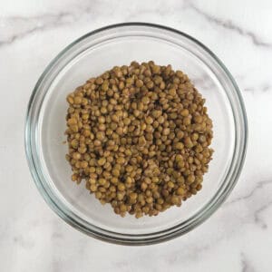 overhead view of glass bowl containing cooked lentils on a marble background