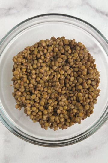 overhead view of glass bowl containing cooked lentils on a marble background