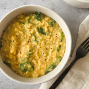 instant pot kitchari in a white bowl with a black fork and cream napkin on a gray stone background