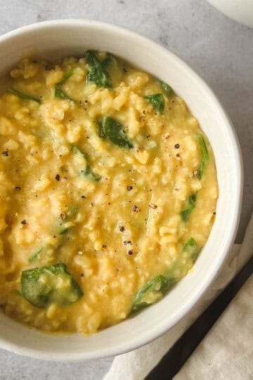 instant pot kitchari in a white bowl with a black fork and cream napkin on a gray stone background