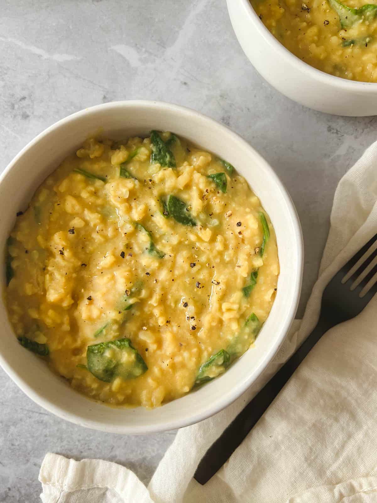 white bowl containing Instant Pot kitchari with a black fork on a gray stone background