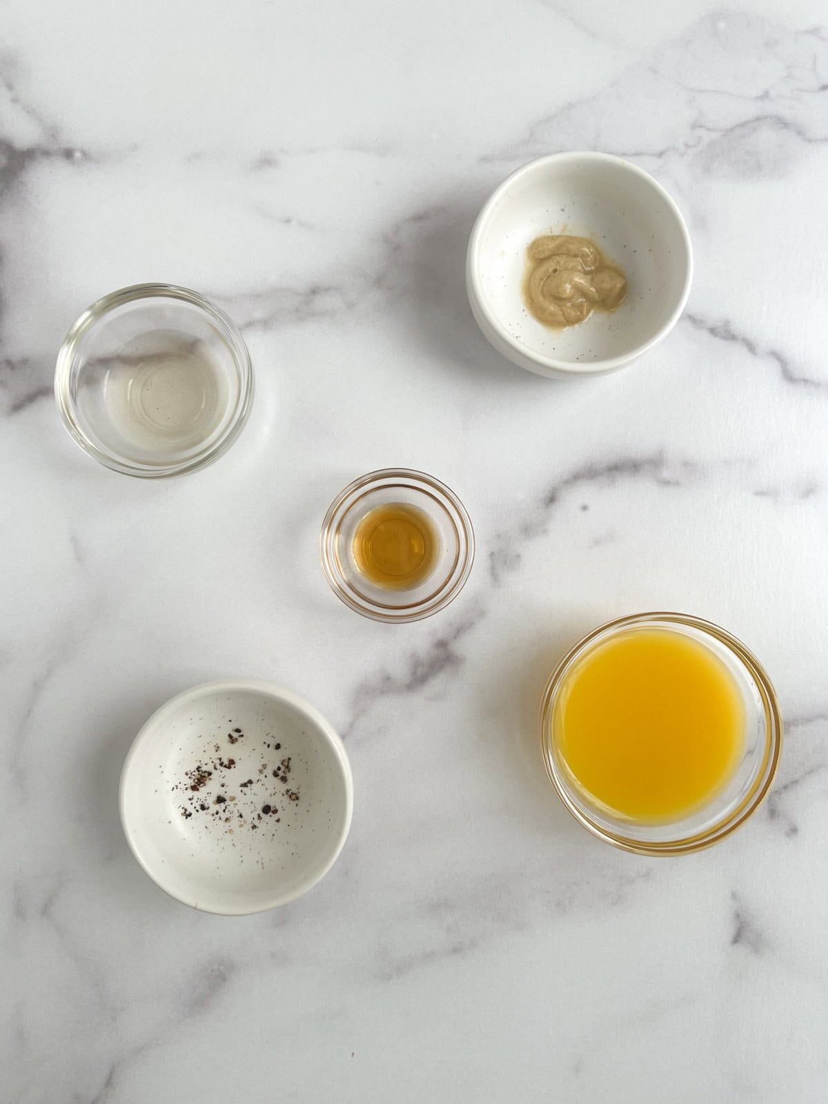 overhead view of ingredients for orange vinaigrette in bowls on a marble background