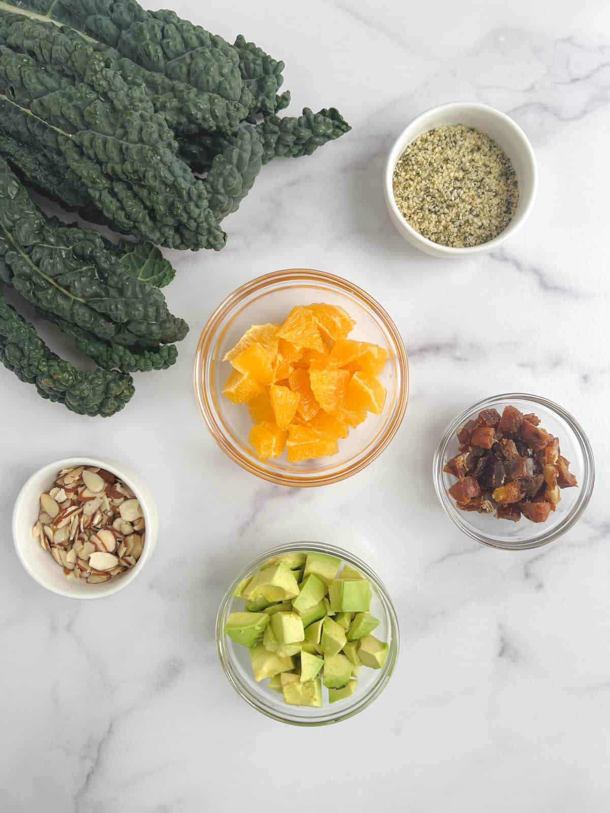 overhead view of ingredients for kale citrus salad in bowls on a marble background