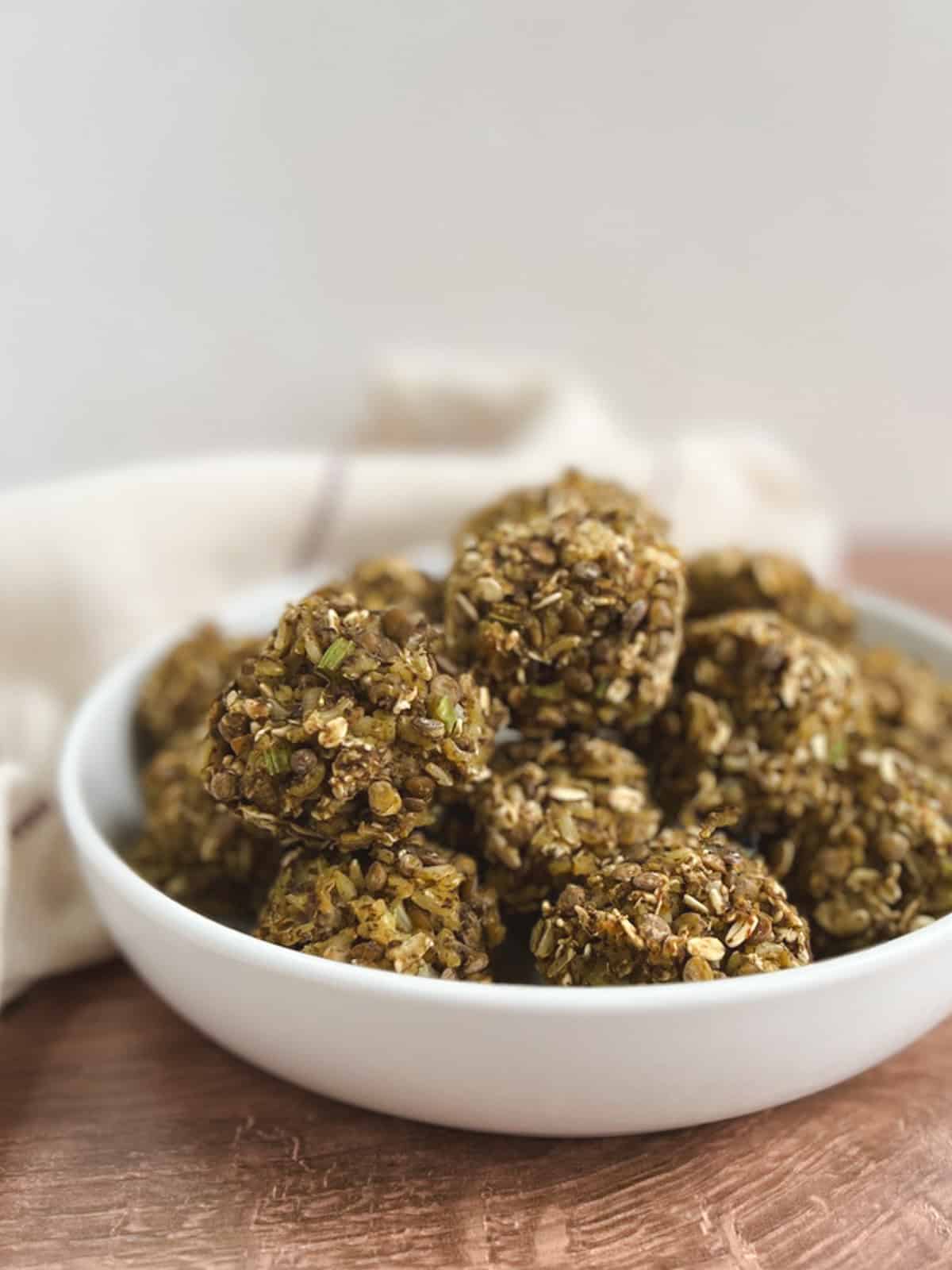 closeup of white bowl containing lentil meatballs with a cream-colored kitchen towel blurred in the background