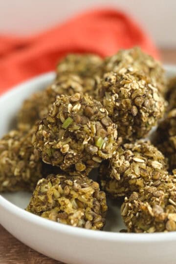 closeup of a white bowl of lentil meatballs with an orange napkin blurred in the background