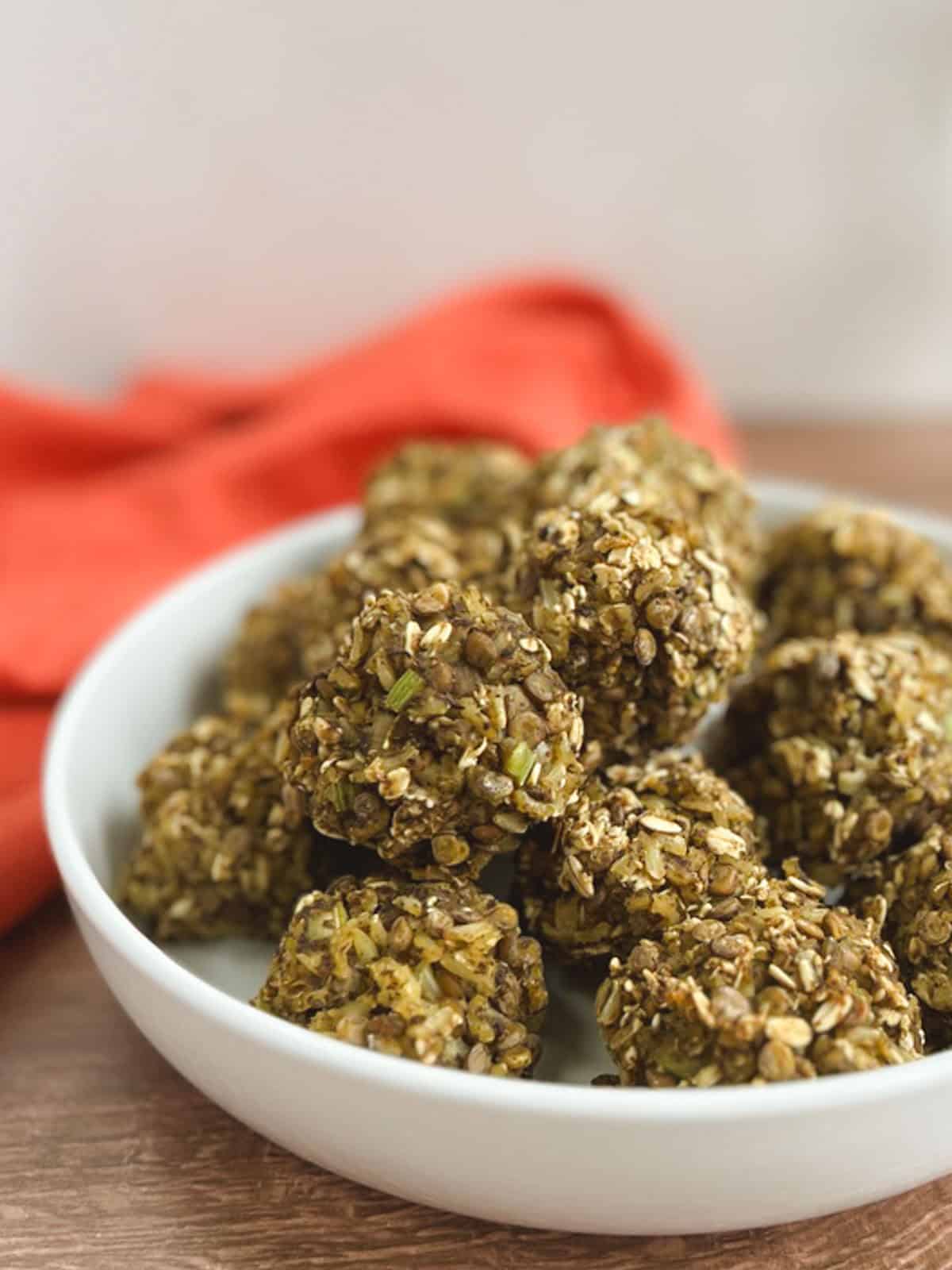 close up of a white bowl filled with lentil meatballs with an orange napkin blurred in the background