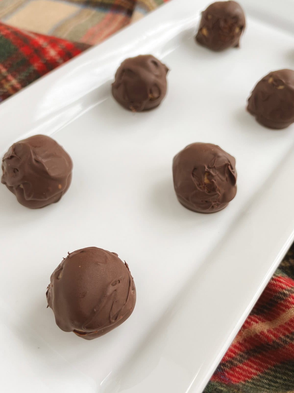 closeup of no bake chocolate peanut butter balls on white rectangular serving tray with plaid background