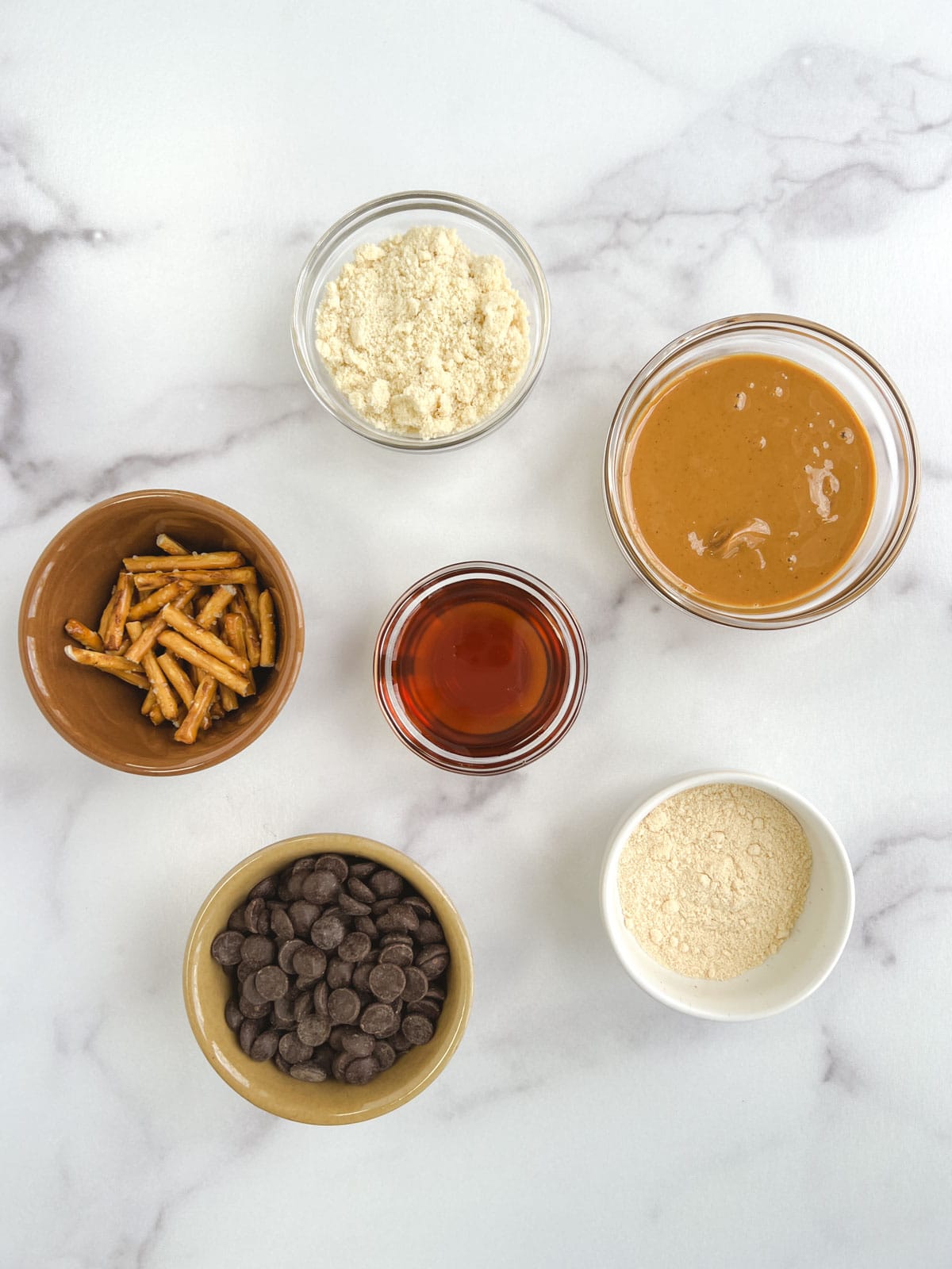 overhead view of bowls containing ingredients for no bake chocolate peanut butter balls on a marble background