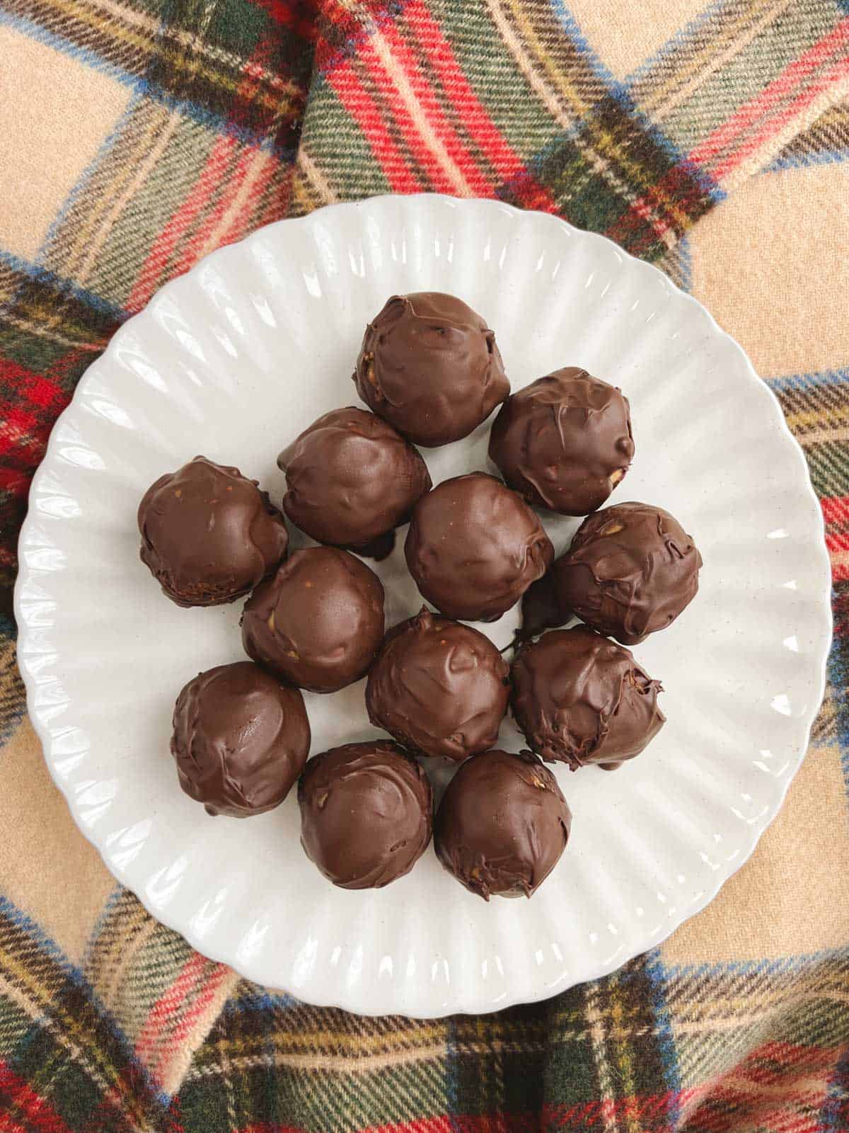 round off-white dish of no bake chocolate peanut butter balls on a plaid background