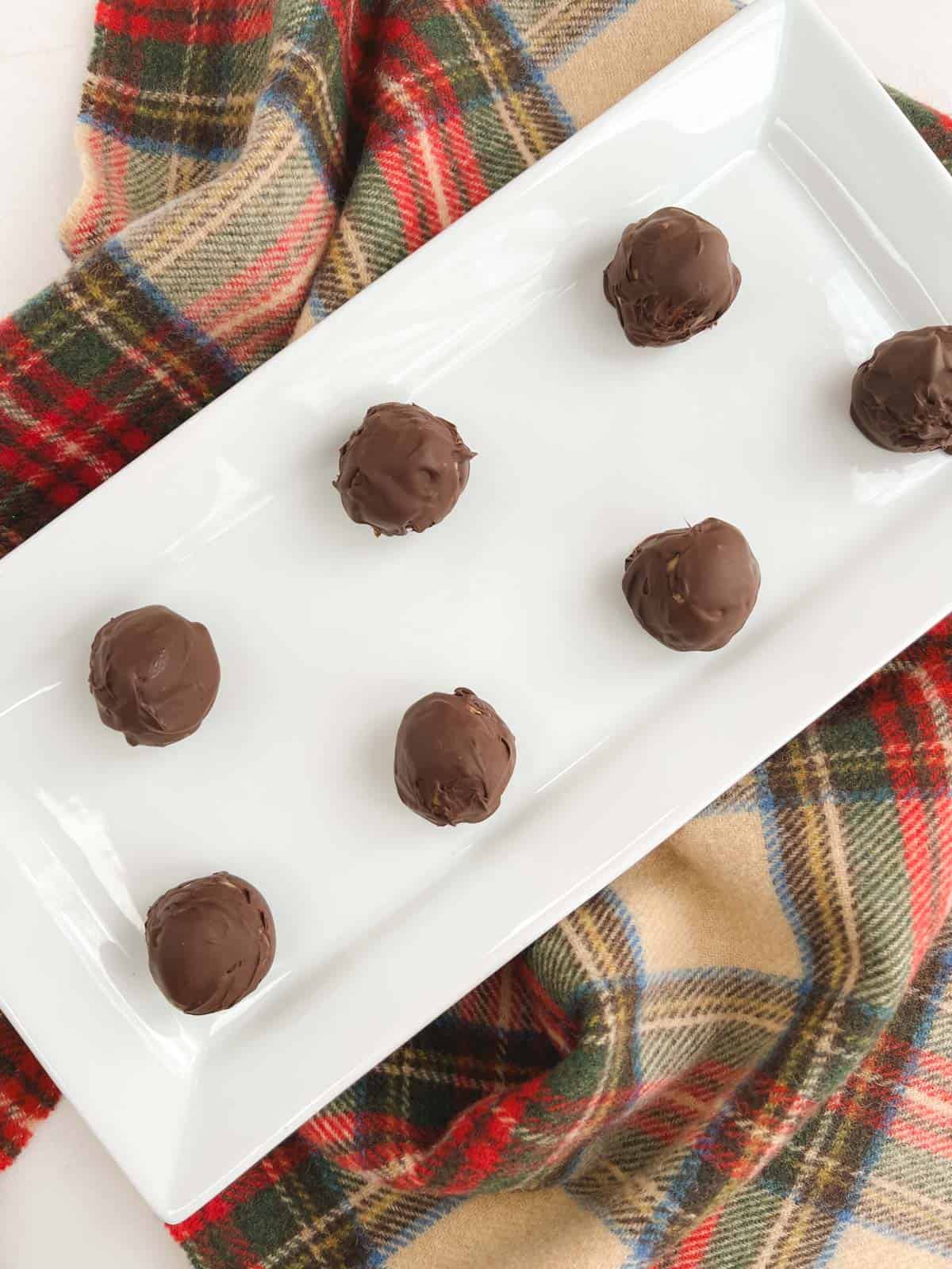 overhead view of rectangular white tray containing no bake chocolate peanut butter balls on a plaid background