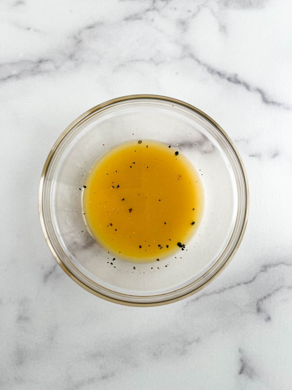 overhead view of glass bowl containing orange vinaigrette on a marble background