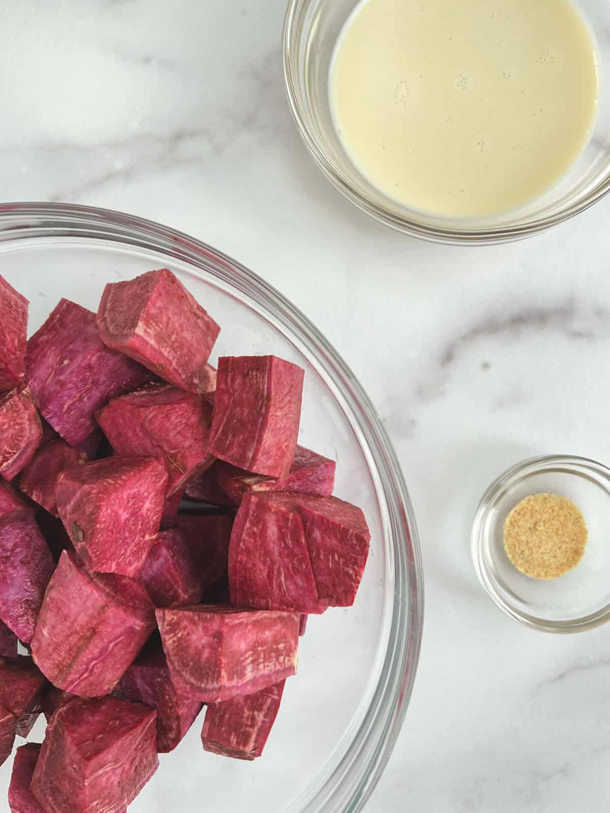 ingredients for purple mashed potatoes in glass bowls on a marble background