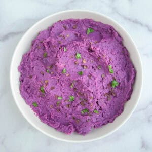 overhead view of a white bowl containing purple mashed potatoes on a marble background