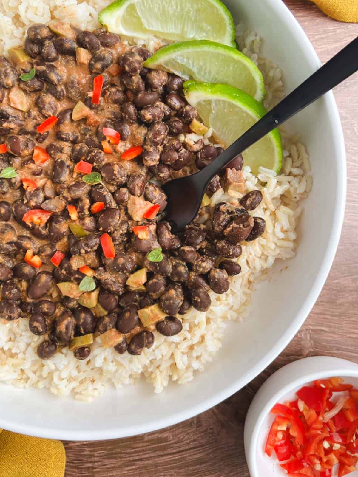 closeup of a bowl of spicy black beans over brown rice garnished with lime slices