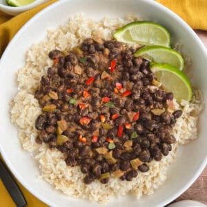 overhead view of white bowl containing spicy black beans over brown rice with lime slices