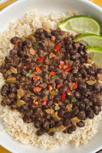 overhead view of white bowl containing spicy black beans over brown rice with lime slices