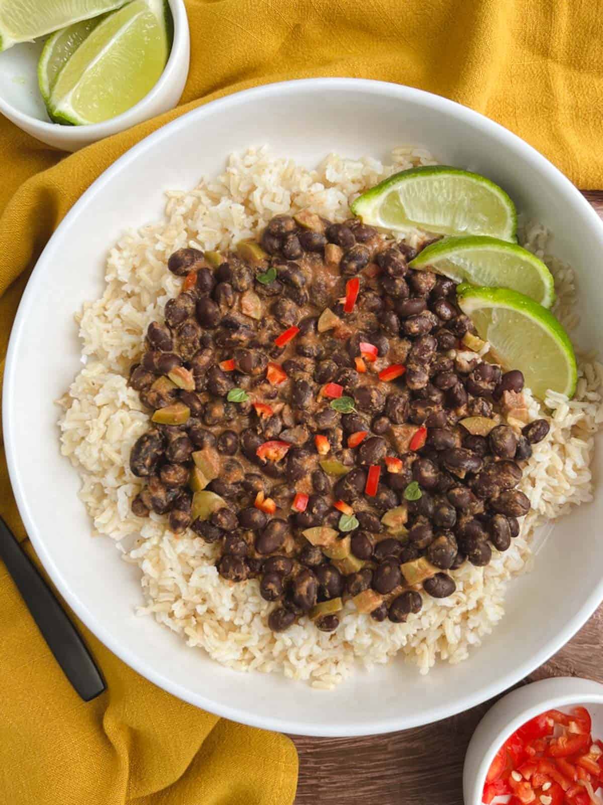 overhead view of white bowl containing spicy black beans over brown rice with yellow napkin in the background