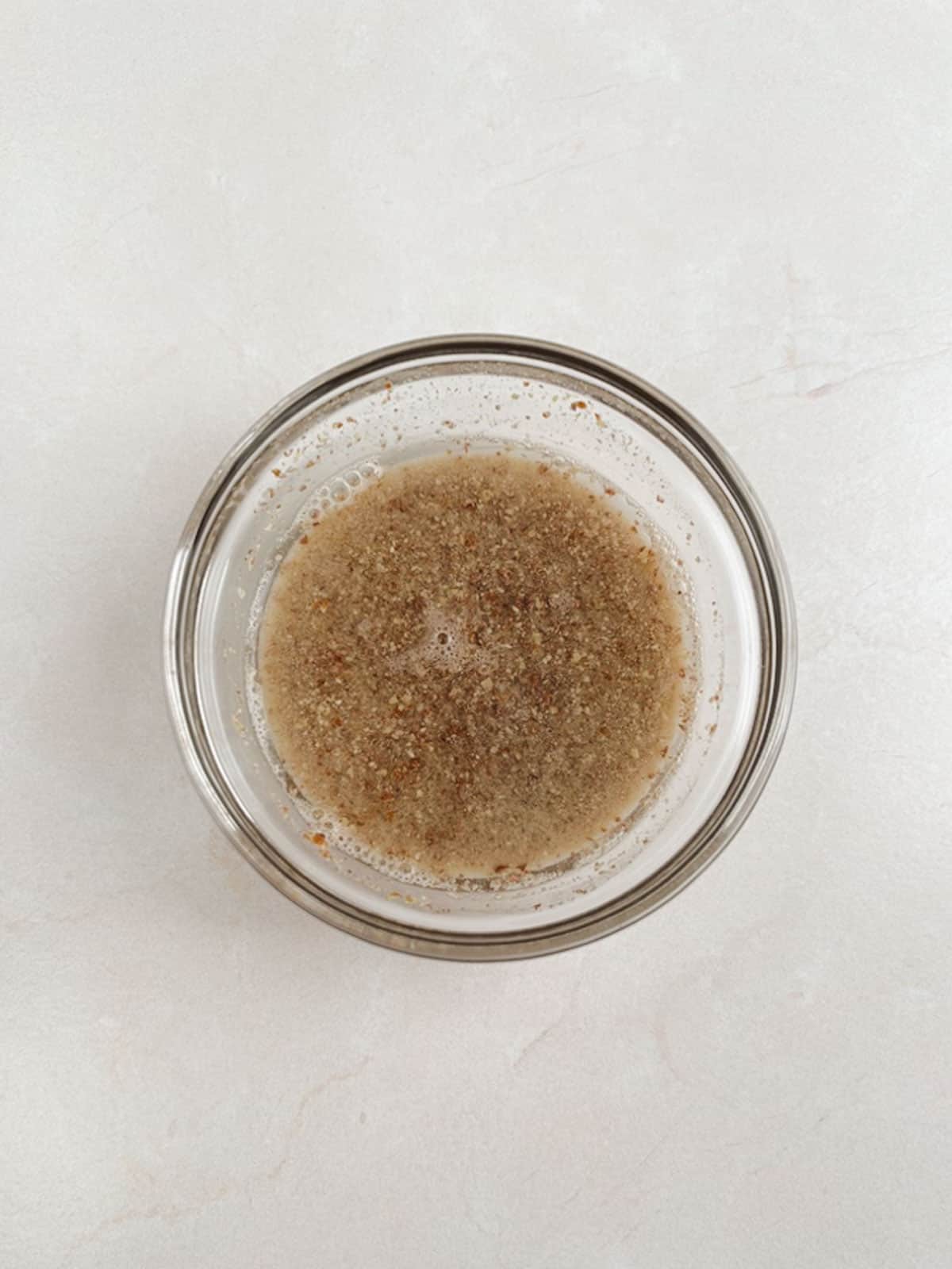 overhead view of a glass bowl containing a flax egg on a white stone background