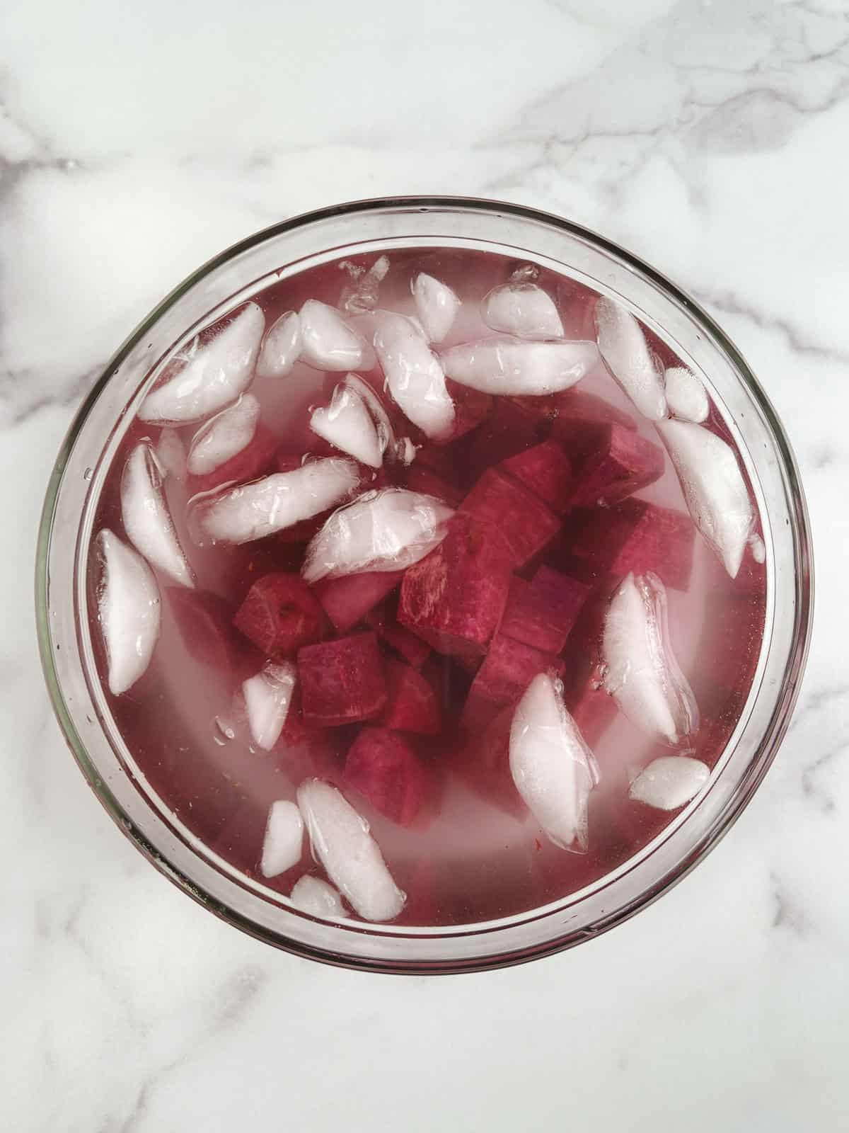 glass bowl containing water with ice cubes and diced raw purple potatoes