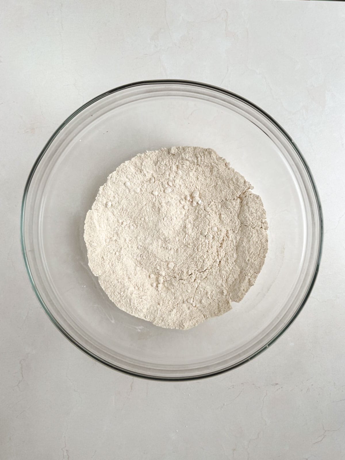 overhead view of a glass bowl containing dry ingredients for apple coffee cake on a white stone background