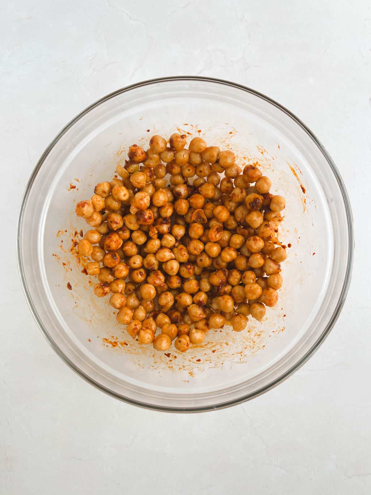 overhead view of glass bowl containing chickpeas coated with harissa paste and black pepper