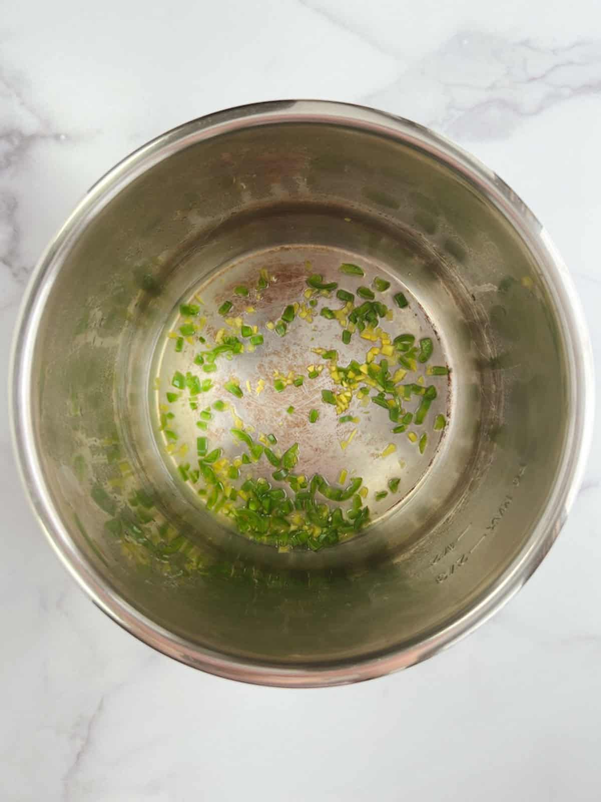 overhead view of Instant Pot inner pot containing cooked serrano pepper and ginger