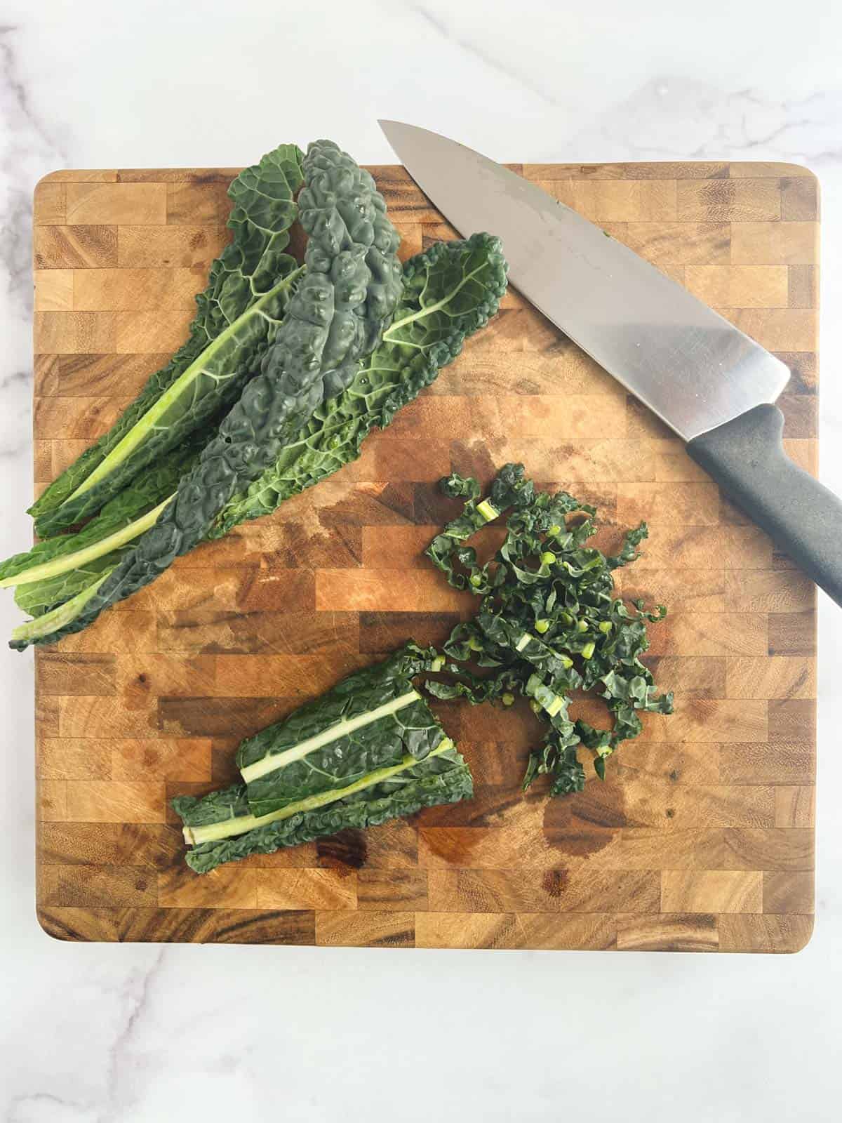 overhead view of cutting board with lacinato kale partially sliced into ribbons next to a chef's knife