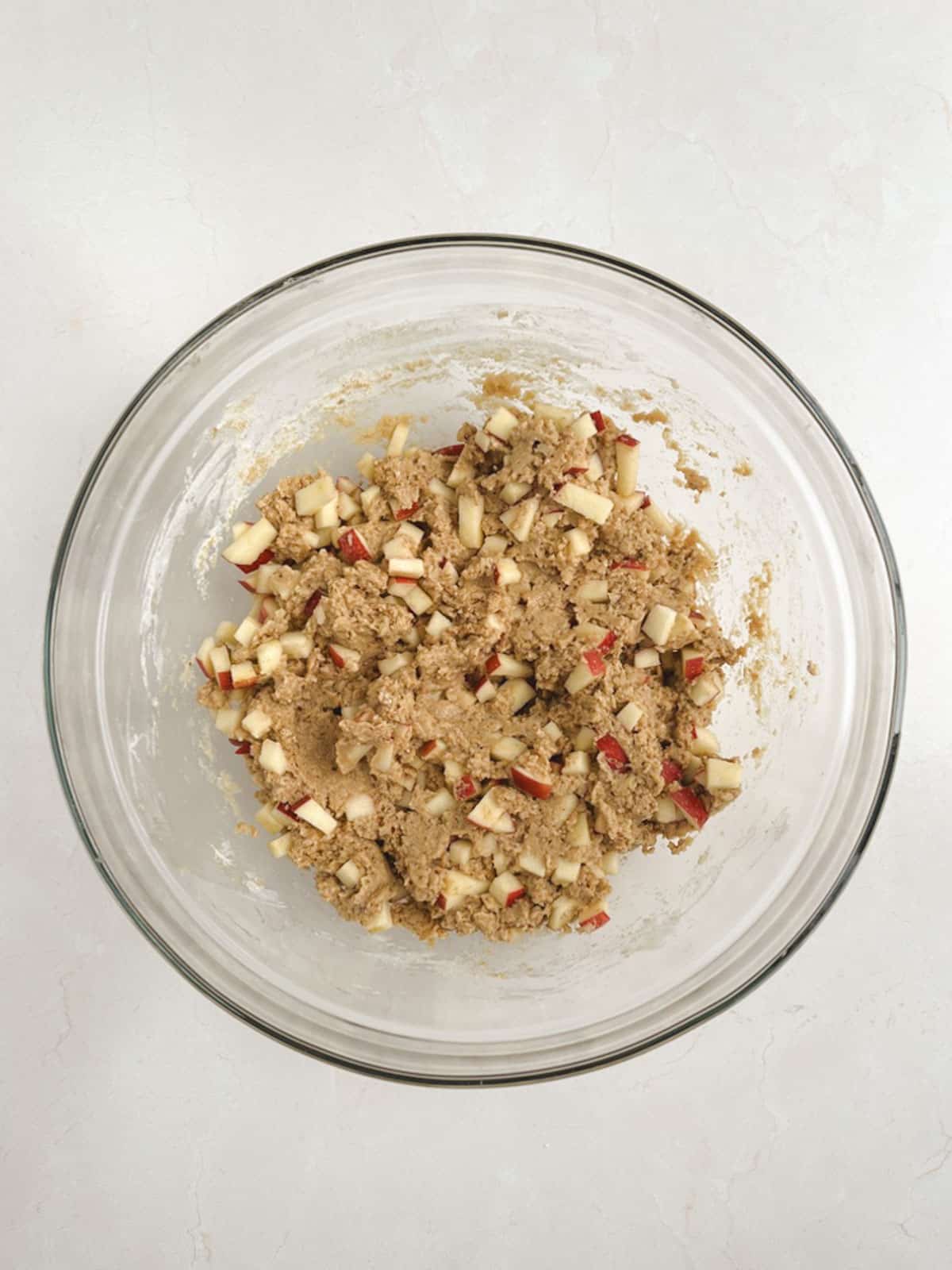 overhead view of a glass bowl containing mixed wet and dry ingredients for apple coffee cake with apple chunks mixed in