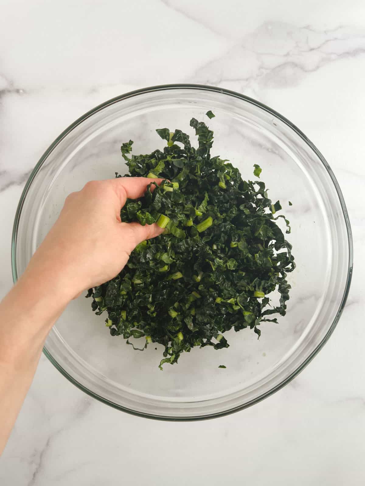 overhead view of kale ribbons in a glass bowl with a hand massaging the kale