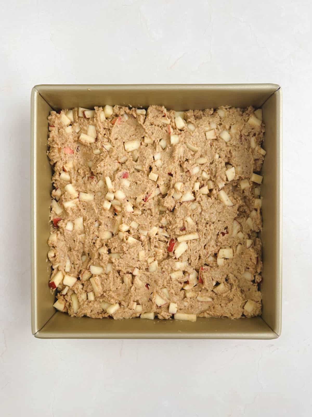 overhead view of a gold square baking pan containing batter for apple coffee cake