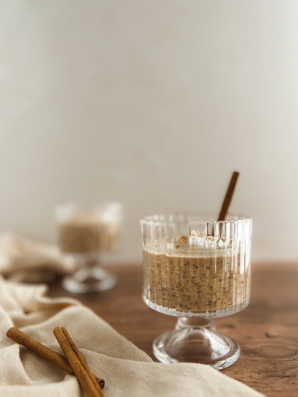 two parfait glasses of chai overnight oats on a wood surface with a linen napkin and cinnamon sticks