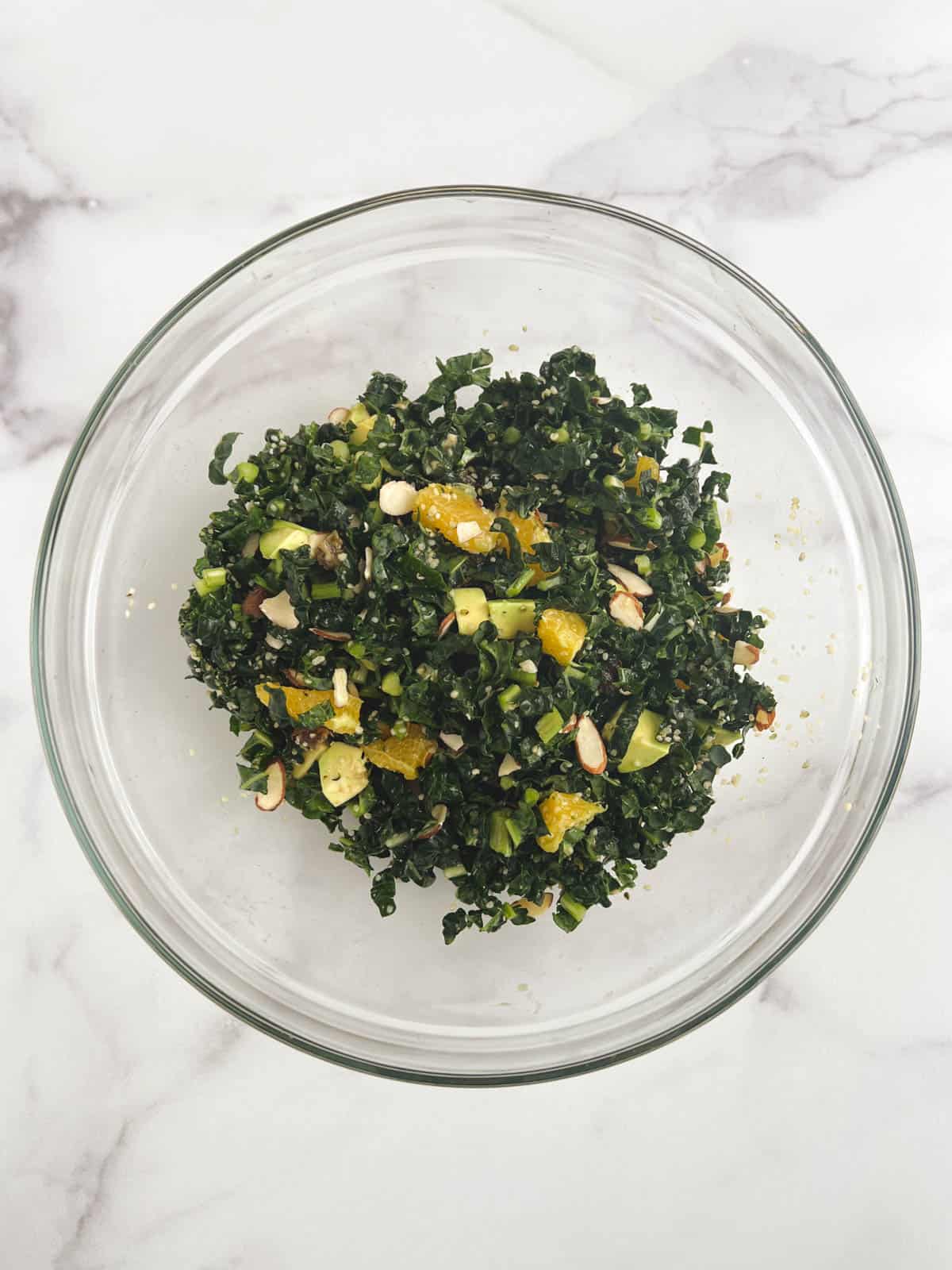 overhead view of glass bowl containing kale citrus salad on a marble background